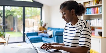 Woman using her laptop sat at her kitchen table at home.